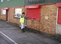 Front elevation of Industrial unit previously coated with a Plastisol paint system. This image shows power washing in progress to remove all loose paints and debris prior to the application of Crown water based metal cladding primer. Weston painting contractors of Cardiff South Wales had to completely removed all traces of dilapidation to all metal sub-straights to obtain maximum substrate adhesion.